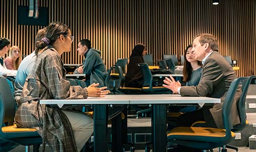 Academic on the right of a table where group of students are meeting and discussing key topics.